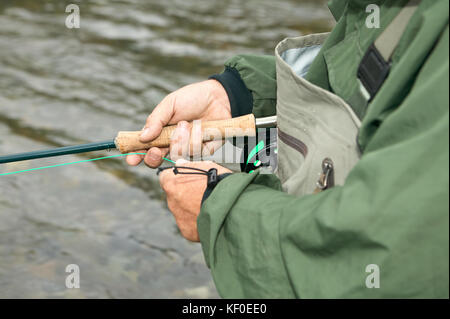 Nahaufnahme Bild eines männlichen fisherman Hände, Haspel und Linie, wie er in einem Süßwasser-stream Fische. Stockfoto