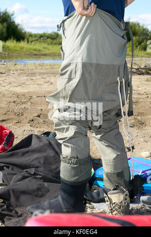 Fischer überstreifen ein Paar waders für Fliegenfischen, wie er unter Campingausrüstung an einem Flussufer steht, niedrigen Winkel Nähe zu sehen, der seine Beine Stockfoto