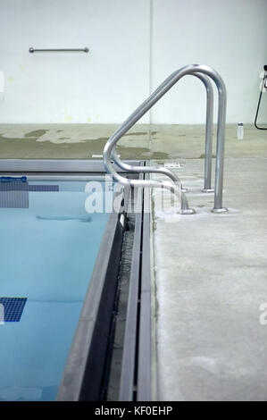 Gebogene metall Geländer Schwimmbad Schritte entlang der Kante auf den Pool und die gepflasterten Surround gesehen Stockfoto