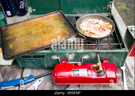 Speck kocht und brutzelt in einer Pfanne bei Gas Campingkocher. Stockfoto