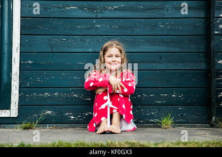 Mädchen mit Bademantel im Freien an Holzhütte mit Spielzeug Windenergieanlage sitzen Stockfoto