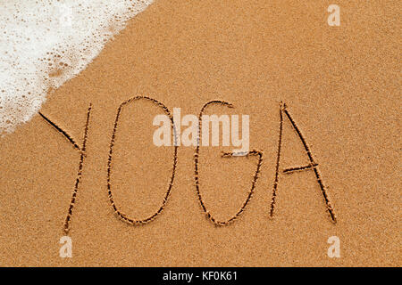 Das Wort Yoga in den Sand des Strandes geschrieben, mit Sea Foam in einer Ecke Stockfoto