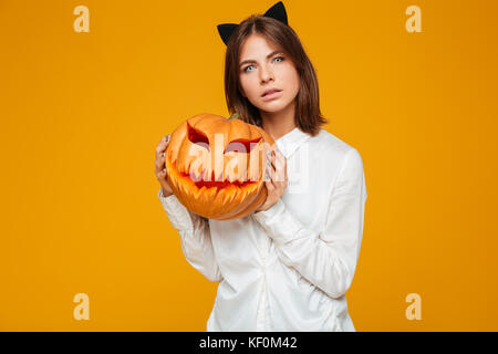 Bild der Schwere junge Frau in Crazy cat Halloween Kostüm auf gelben Hintergrund mit Kürbis gekleidet. Stockfoto