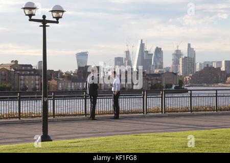 Die Arbeiter entspannen sich während ihrer Tee- und Kaffeepausen in der Herbstsonne am Canary Wharf mit Blick auf die Themse und die City of London. Stockfoto