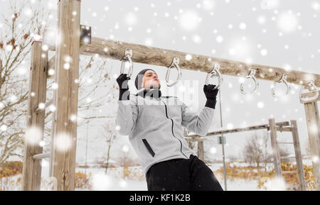 Junger Mann Ausübung auf horizontalen Balken im Winter Stockfoto