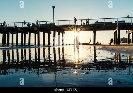 Silhouette Menschen auf und unter dem Brighton Beach Pier auf Coney Island mit Sunburst Stockfoto