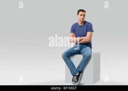 Junge Mann sitzt auf White Cube. isoliert. Platz für Text Stockfoto