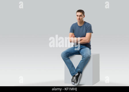 Junge Mann sitzt auf White Cube. isoliert. Platz für Text Stockfoto