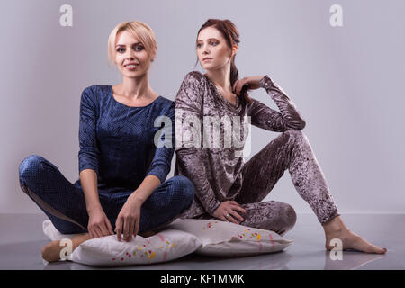 Zwei Frauen in den Schlafanzügen sitzen auf Kissen auf einem grauen Hintergrund. Studio shoot Stockfoto