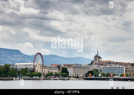 Blick auf die Rhône und die Altstadt mit der Kathedrale St. Peter und ein Riesenrad am Ufer unter einem bewölkten Himmel. Genf, Schweiz. Stockfoto