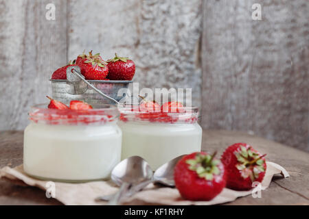 Joghurt mit Marmelade Sauce in Glas und einen Eimer mit frischen Erdbeeren auf einer hölzernen Hintergrund. Stockfoto