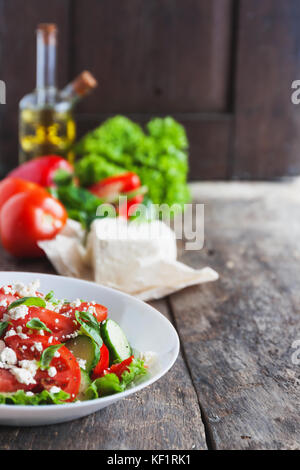 Shopska Salat in eine weiße Platte auf einem hölzernen Hintergrund, eine Reihe von Zutaten Salat Stockfoto