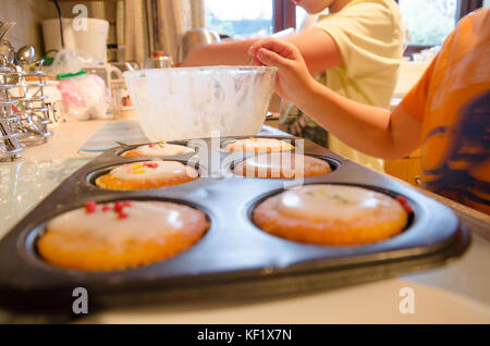 Ein paar der jungen Brüder frisch gebackene Cupcakes mit Zuckerglasur verzieren und Streuseln. Stockfoto