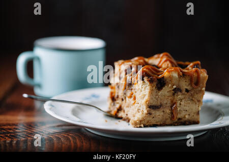 Brotpudding mit Karamell Sauce serviert mit einer Tasse heißen Kakao auf dunklen rustikalen Hintergrund Stockfoto