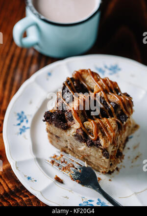 Brotpudding mit Karamell Sauce serviert mit einer Tasse heißen Kakao auf dunklen rustikalen Hintergrund Stockfoto