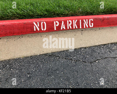 Red stenciled kein Parkplatz Zone bändigen Schild mit grünem Gras und Asphalt Stockfoto