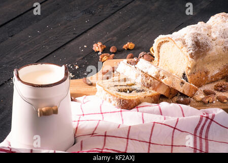 Herzhafte hausgemachte Pound Cake mit Mohn, Nüssen und Mandeln, und einem antiken Eimer Milch, auf einem schwarzen Holztisch. Stockfoto