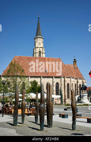 Die St.-Michael-Kirche am Unirii Square, gesehen von der Ecke der Piata Unirii und Strada Napoca, Mädchen sitzt auf der Bank im Vordergrund Stockfoto