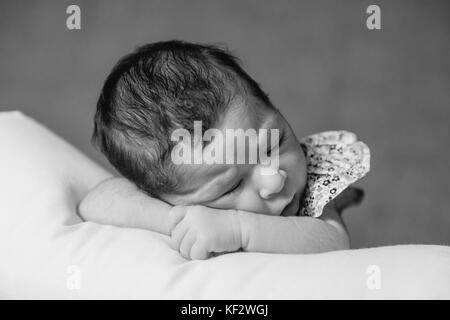 Nahaufnahme, Porträt einer niedlichen Zwei Wochen alte Neugeborene Mädchen mit einem geblümten Kleid, schlief friedlich über ein Kissen/Neugeborenen baby portrait cute Stockfoto