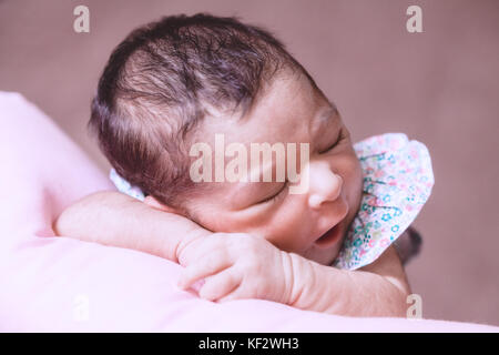 Nahaufnahme, Porträt einer niedlichen Zwei Wochen alte Neugeborene Mädchen mit einem geblümten Kleid, schlief friedlich über ein Kissen/Neugeborenen baby portrait cute Stockfoto