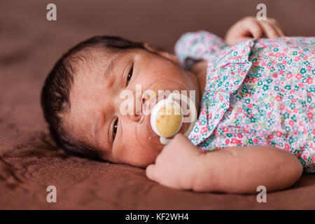 Nahaufnahme, Porträt einer niedlichen Zwei Wochen alte Neugeborene Mädchen mit einem geblümten Kleid mit verschlafenen Augen/Neugeborenen baby portrait cute girl schläfrig schläfrig Stockfoto