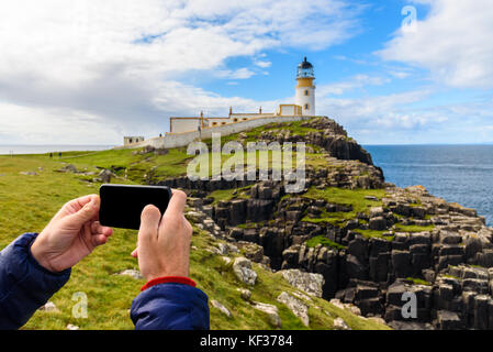 Ein Mann Fotografien die neist Point Lighthouse in der Isle of Skye in Schottland mit seinem Smartphone. Stockfoto