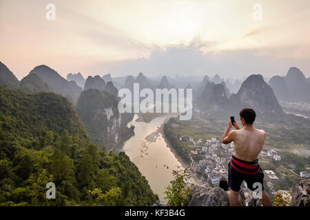 Xingping, China - 18. September 2017: unbekannter Mann nimmt Bild mit einem Mobiltelefon von Li River View bei Sonnenuntergang. Stockfoto