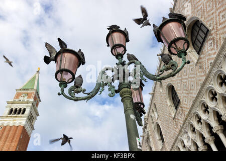 Venedig, Blick auf eine Straßenlaterne mit Tauben fliegen in St. Markusplatz mit Dogenpalast und der Glockenturm im Hintergrund Stockfoto