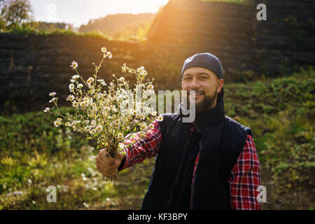 Stilvolle hipster Mann hält Herbst Strauß Wildblumen in sonnige Landschaft und wartet. Platz für Text. Rustikale Bräutigam mit einfachen Blumen in den Händen. Stockfoto