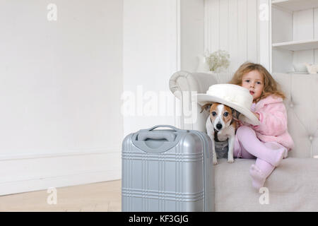 Ein kleines Mädchen mit Koffer und ein Hund im Innenraum Stockfoto