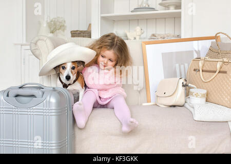 Ein kleines Mädchen mit Koffer und ein Hund im Innenraum Stockfoto