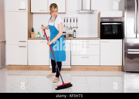 Junge cleaner Hausmädchen fegen Stock mit Besen in Küche Stockfoto