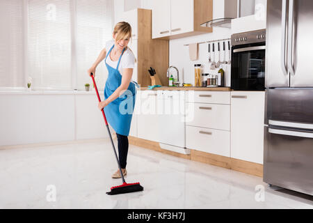 Junge Hausmädchen Reinigung Boden mit Besen in Küche Stockfoto