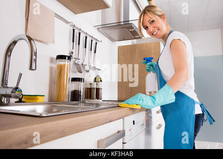 Lächelnden jungen Reiniger Frau mit Schürze Reinigung verschmutzter Küchenarbeitsplatte Stockfoto
