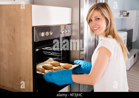 Junge lächelnde Frau mit Backblech aus Mikrowelle Stockfoto