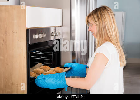 Junge lächelnde Frau mit Backblech aus Mikrowelle Stockfoto