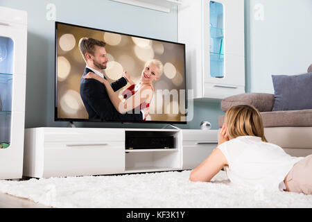 Junge Frau Liegt Auf Dem Teppich Und Schaut Sich Zu Hause Einen Romantischen Film Im Fernsehen An Stockfoto