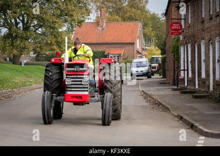 Mann, der alte rot vintage MF-Traktor durch Dorf Bugthorpe auf Wolds Vintage Gruppe Straße laufen, eine jährliche Charity Event - Yorkshire, England, UK. Stockfoto