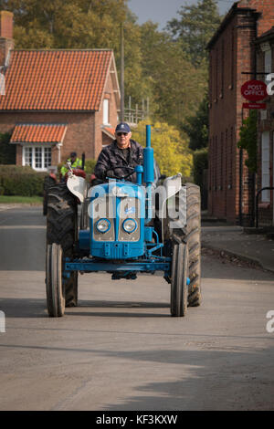 Mann, der Blue vintage Traktor in eine Parade durch Bugthorpe Dorf für die jährliche Charity Event-Wolds Vintage Gruppe Straße laufen, Yorkshire, England, UK. Stockfoto