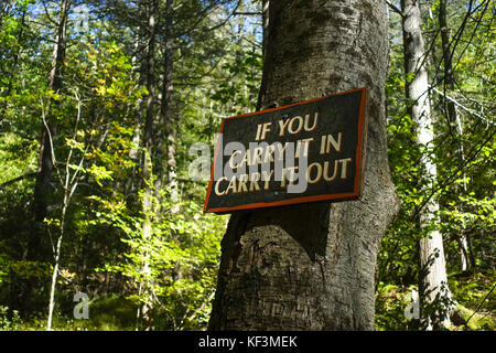 Zeichen: 'Wenn Sie es in Carry It Out' tragen. nehmen Sie ihren Müll zu Hause, hölzernes Schild am Baum. Bushkill Falls, USA. Stockfoto