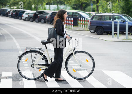 Seitenansicht der junge lächelnde Geschäftsfrau mit Handtasche das Pendeln mit dem Fahrrad Stockfoto