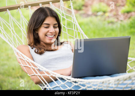 Lächelnden jungen Frau liegend auf Hängematte mit Laptop Stockfoto