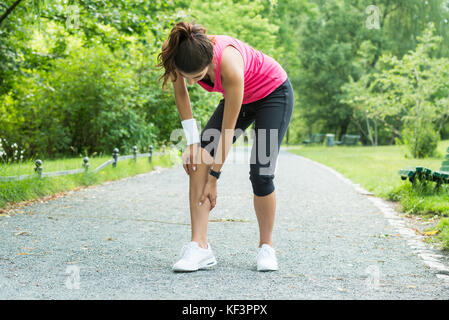 Junge weibliche Jogger in Schmerz in ihrem Bein im Park Stockfoto