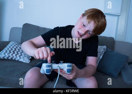 Unglückliche Junge sitzt auf einem Sofa drücken der Taste des Joysticks Stockfoto