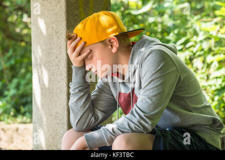 Verärgert Junge sitzt im Park mit der Hand auf den Kopf Stockfoto