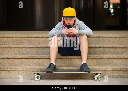 Junge sitzt auf Treppe tragen Cap am Handy suchen Stockfoto