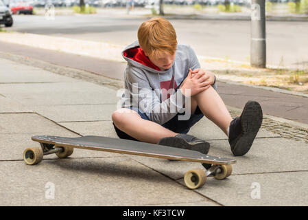 Junge Blick auf Sein verletztes Bein sitzen in der Nähe von Skateboard Stockfoto