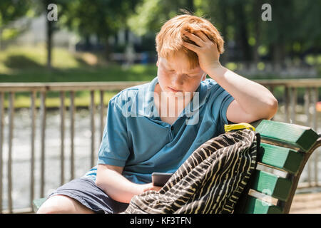 Schüler sitzt auf der Bank am Handy suchen Stockfoto