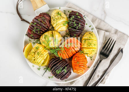 Ideen von veganes Essen, Herbst Rezepte aus Gemüse. gerösteten hasselback rote Rüben, Karotten, Kartoffeln, mit frischen Kräutern, auf einen Teller, auf weissem Marmor zurück Stockfoto