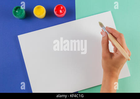 Frau hand mit Malerei Pinsel, Aquarellfarben und ein leeres Blatt Papier. Stockfoto
